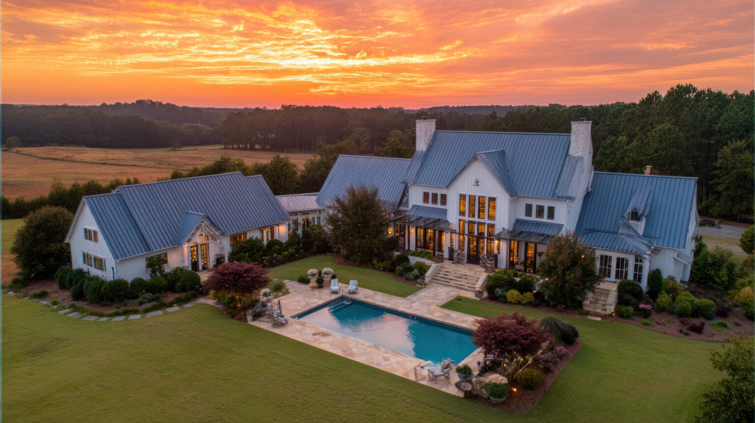 Lake Lanier Real Estate: An aerial view showcases a grand residential structure featuring a swimming pool, set against a colorful sunset. The exterior displays architectural details, surrounding greenery, and a reflective pool surface. This image is suitable for various commercial uses, including real estate, architecture, or lifestyle content.